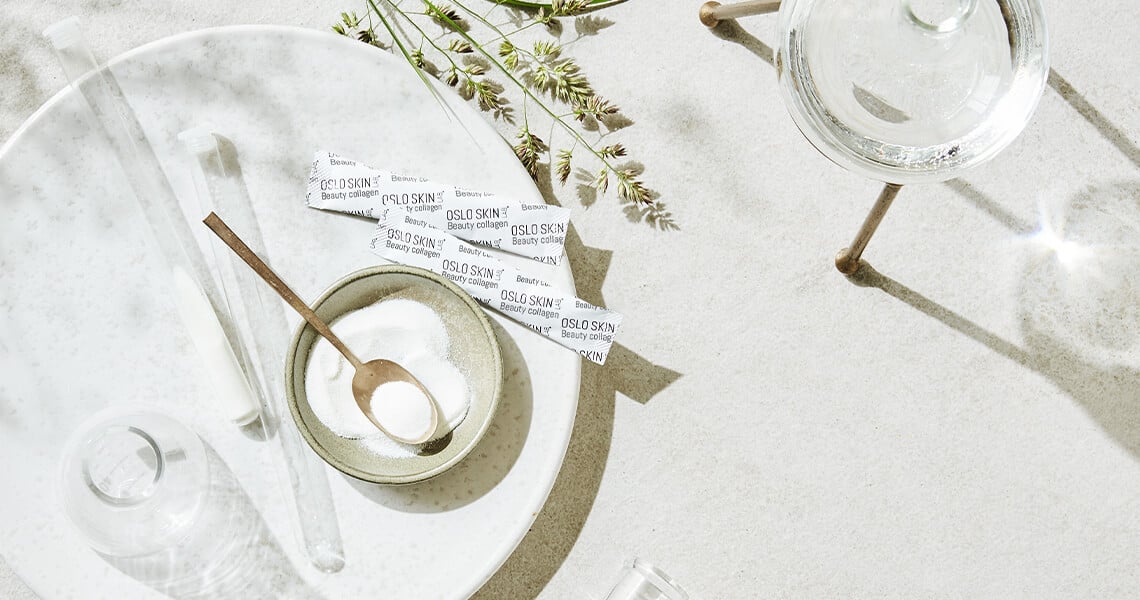 pytlíčky kolagenu The Solution na mramorové kuchyňské lince, vedle sklenice s vodou