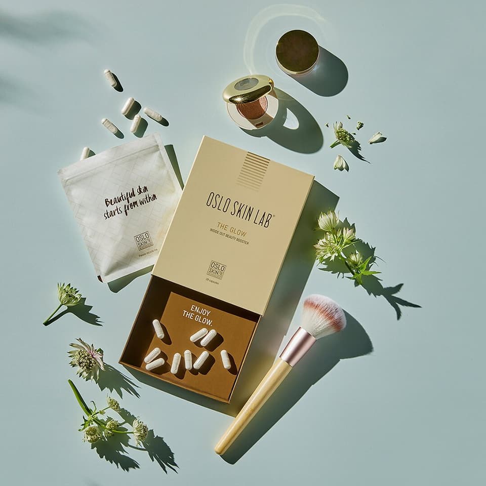 otevřené balení The Glow, položené na stole, tablety okolo balení, další kosmetické produkty položené u The Glow