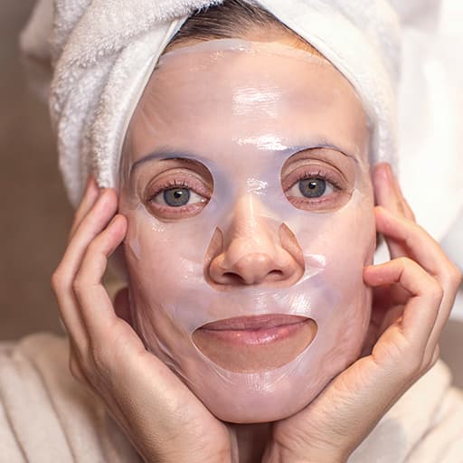 Žena s maskou The Glow Up umístěnou na obličeji, dívá se do kamery