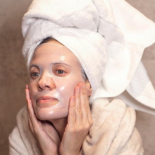 žena má na obličení aplikovanou masku The Hydro Bomb a dívá se do zrcadla v koupelně, má ručník na hlavě